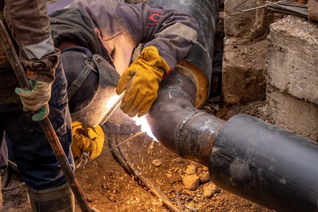 Worker welding a large steel pipe in an excavation